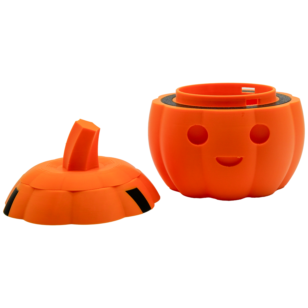 Kürbis-Behälter von vorne in orange. Mittig: zwei kleine als Augen und unterhalb davon einen Halbkreis als Mund. Der Deckel mit dem Stiel ist abgenommen und liegt links von dem Behälter. 