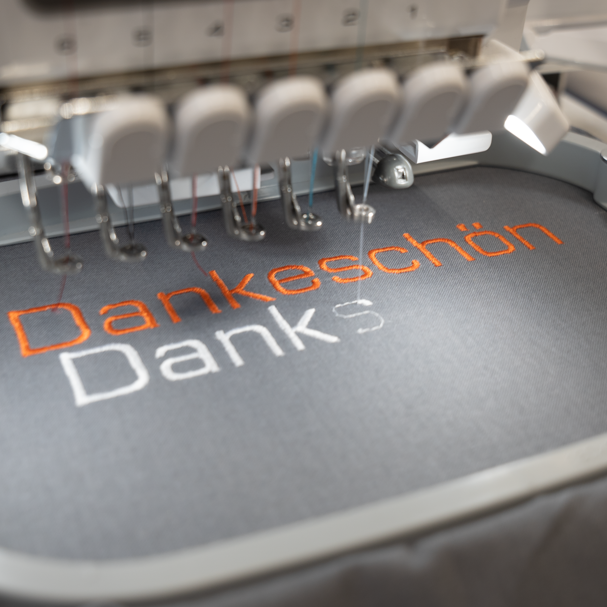 Stickmaschine, die "Dankeschön" auf eine graue Stofftasche stickt.